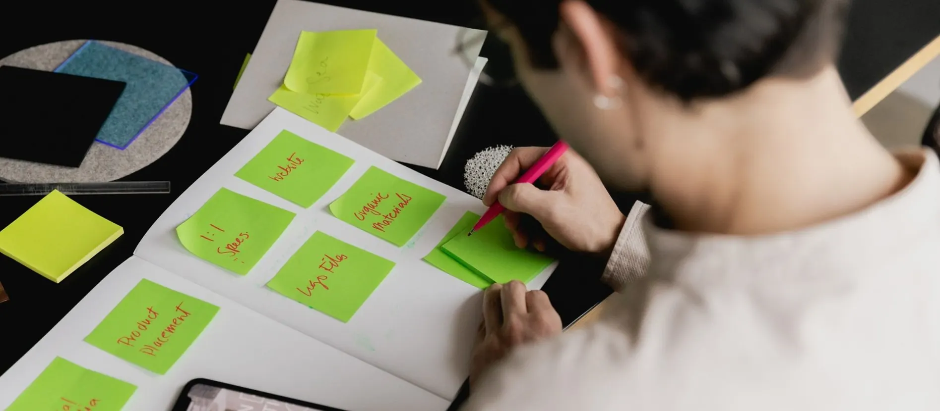 Een hand schrijft op groene plakbriefjes die op een schrijfblok liggen