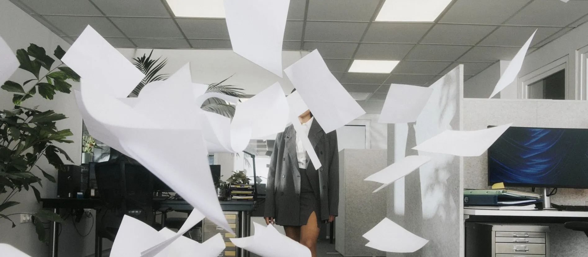 Een kantoor waarin losse vellen papier door de lucht vliegen, met een collega op de achtergrond