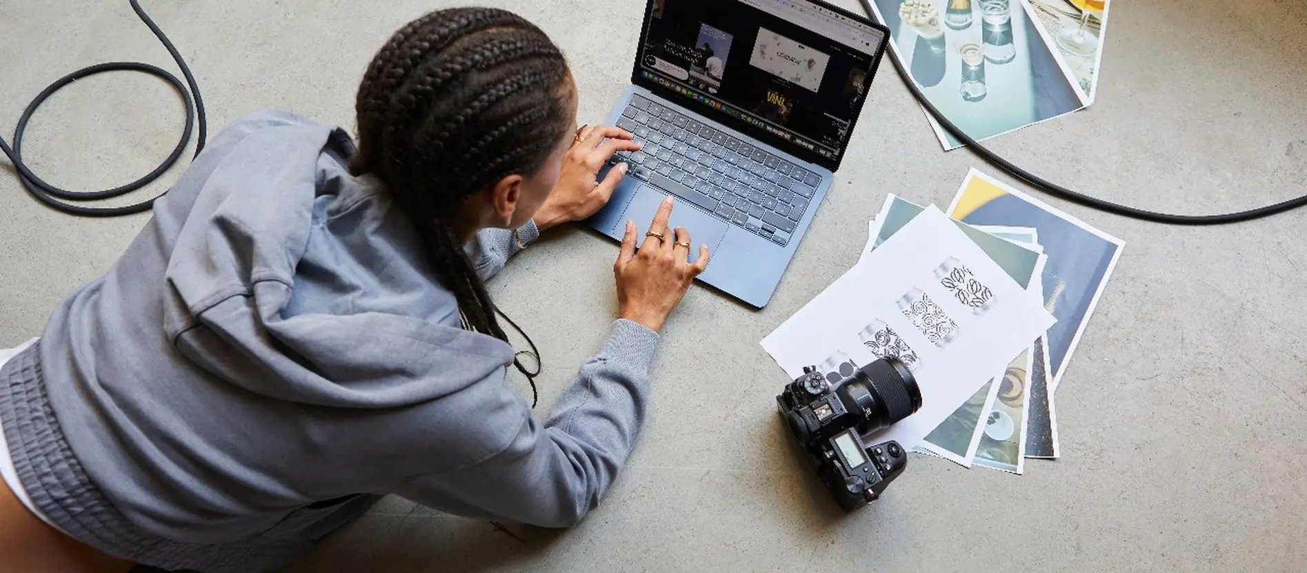 Ontwerpster op de vloer met laptop, uitgeprinte foto's en een camera